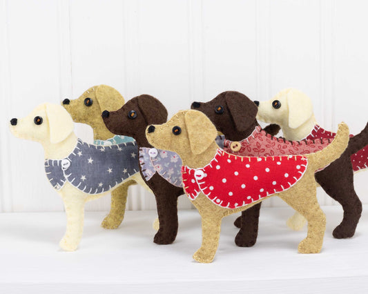 A group of felt Labrador ornaments including golden, cream, chocolate and black Labradors, wearing cotton print jackets in a variety of colours.