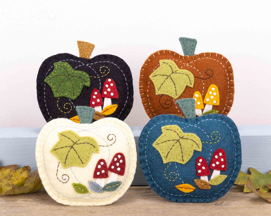 Group of 4 pumpkin felt ornaments, each appliqued and embroidered with leaves, stems and small red toadstools with white spots. The pumpkin background colours are black, rust, cream and teal.